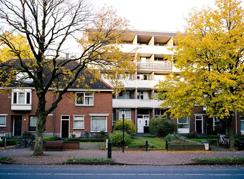 Rijtjeshuizen met voortuinen en fietsen, met daarachter een flat van vijf verdiepingen met galerijen, in de herfst